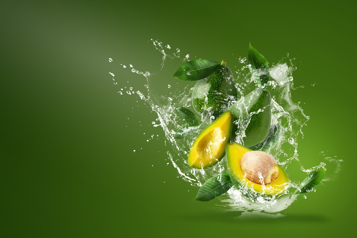 Water splashing on fresh sliced green avocado over green background. 