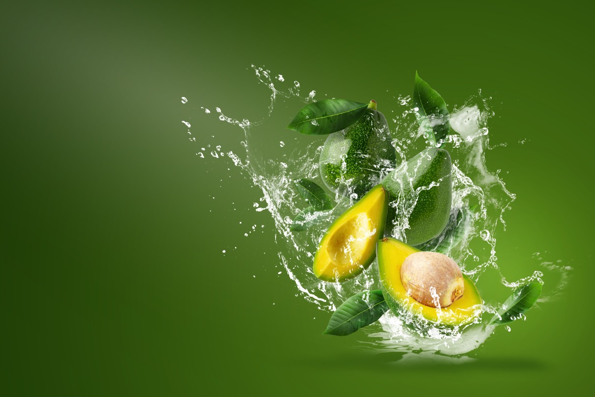 Wasser spritzt auf frisch aufgeschnittene grüne Avocados auf grünem Hintergrund.