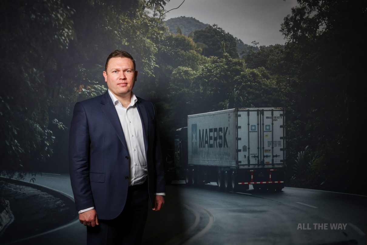 Photo of a man in front of a screen, a truck in the background.