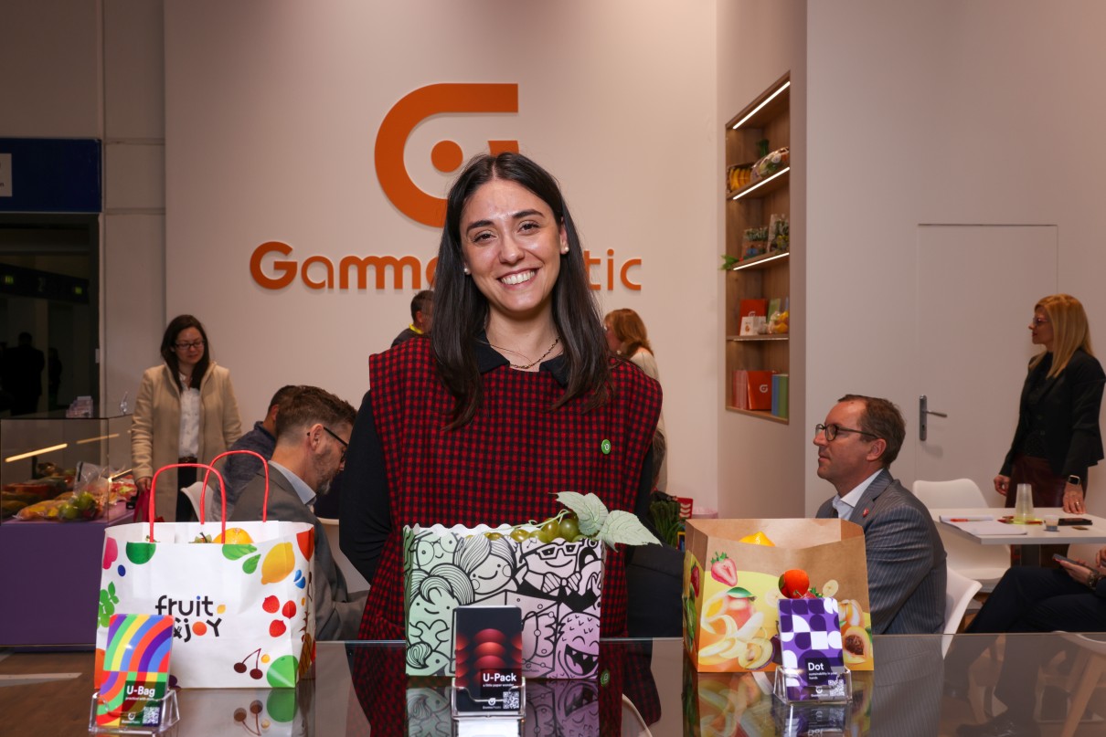 A smiling woman behind a table with several colourful paper bags on it